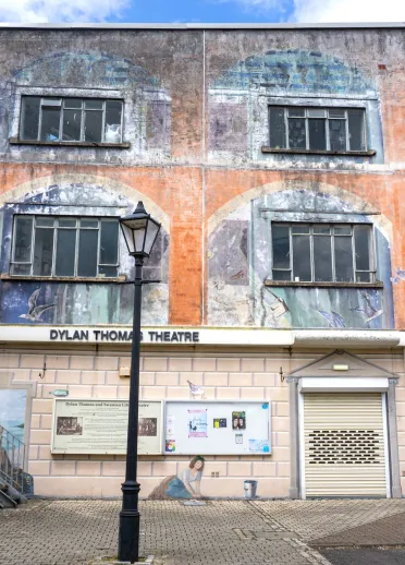 Exterior of a theatre building with faded murals on the walls.