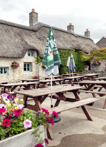 Outdoor seating area with picnic benches beside the thatched Blue Anchor Inn in Aberthaw