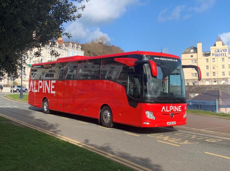 A red coach parked on the promenade of a seaside resort.