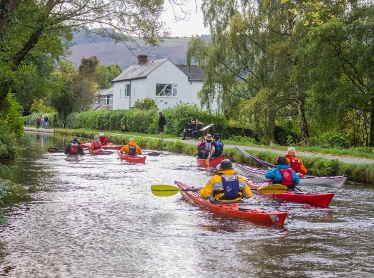 A group of people canoeing down a river in colourful protective waterproofs.