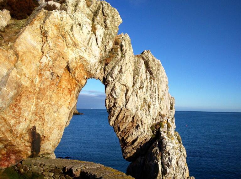 Natürlicher Felsbogen in einer Klippe mit blauem Meer dahinter.