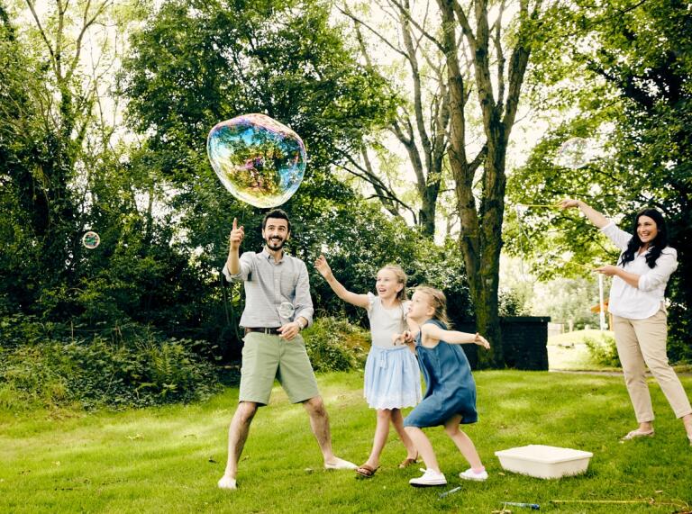 Eltern und zwei Mädchen haben Spaß bei der Jagd nach großen Seifenblasen.