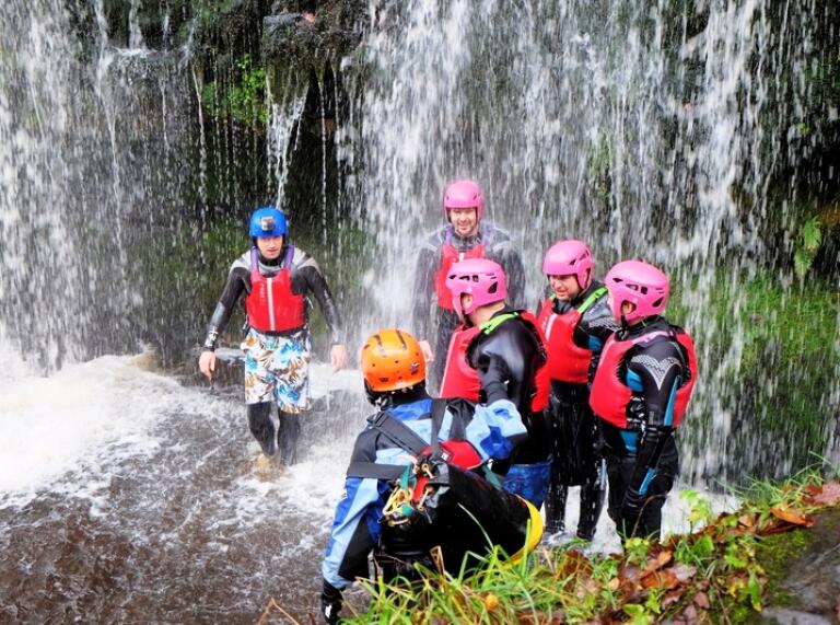 A group of people under a waterfall wearing safety gear.