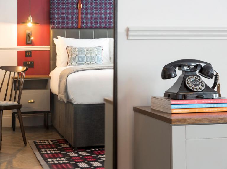 A hotel bedroom with an adorned with Welsh tapestry fabrics and an old phone.