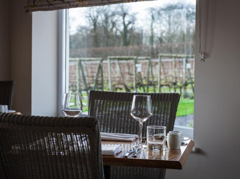 A table set for dining next to a window with views over a vineyard.