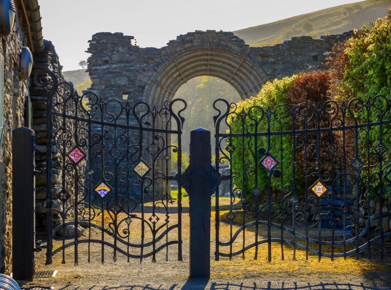 Schmiedeeiserne, mit keltischen Symbolen verzierte Tore vor einem Torbogen einer Abtei-Ruine.