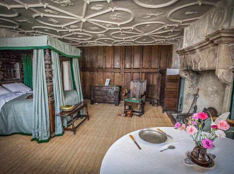 An Elizabethan bedroom with a four poster bed, ornate ceiling and grand fireplace.