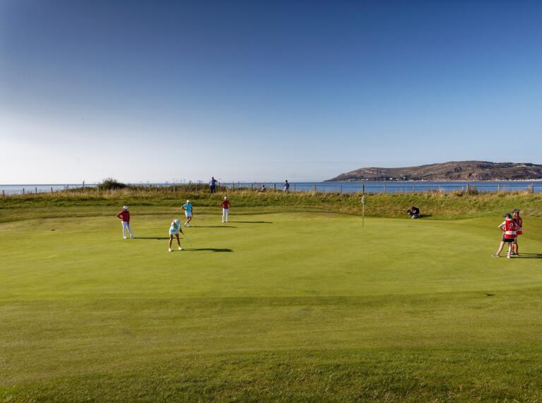 Golfers putting on a green with views of the coastline beyond.