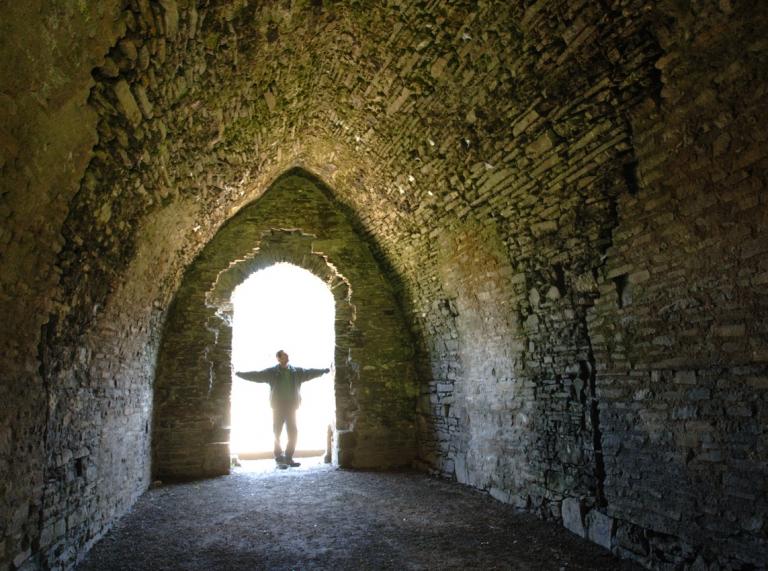 Silhouette eines Mannes, der in ein altes, von Steinmauern umgebenes Verlies blickt.