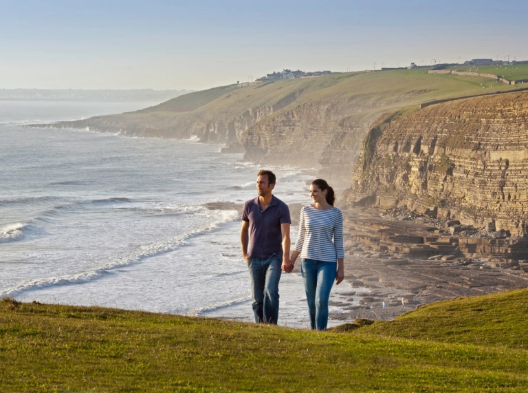 A couple walking on a coastal path with jurassic cliffs beyond.