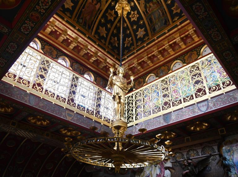 An ornate ceiling and fixture depicting a golden statue in a castle.