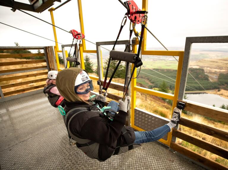 Two people at the top of a seated zip line ready to launch.