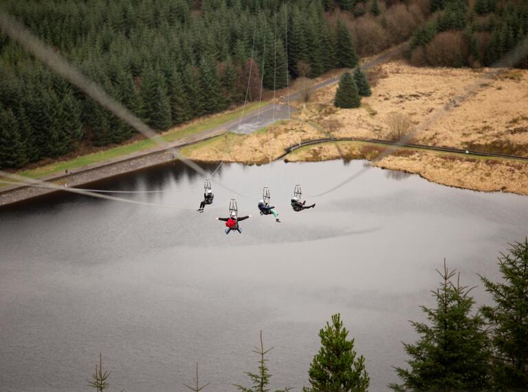 Vier Personen auf einer Seilrutsche über einem See.