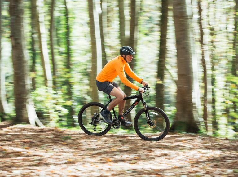 Biker in orange shirt riding a mountain bike along a track in woodland.