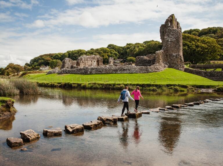 People walking on stepping stones over an estuary toward a castle.