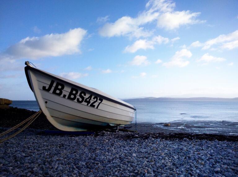 Small white row boat on a pebble beach with sea in the background