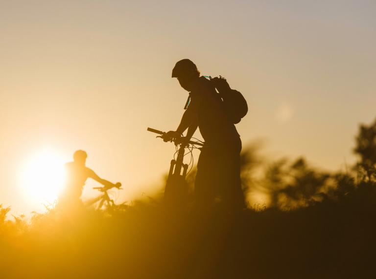 Silhouette of two people standing with their mountain bikes