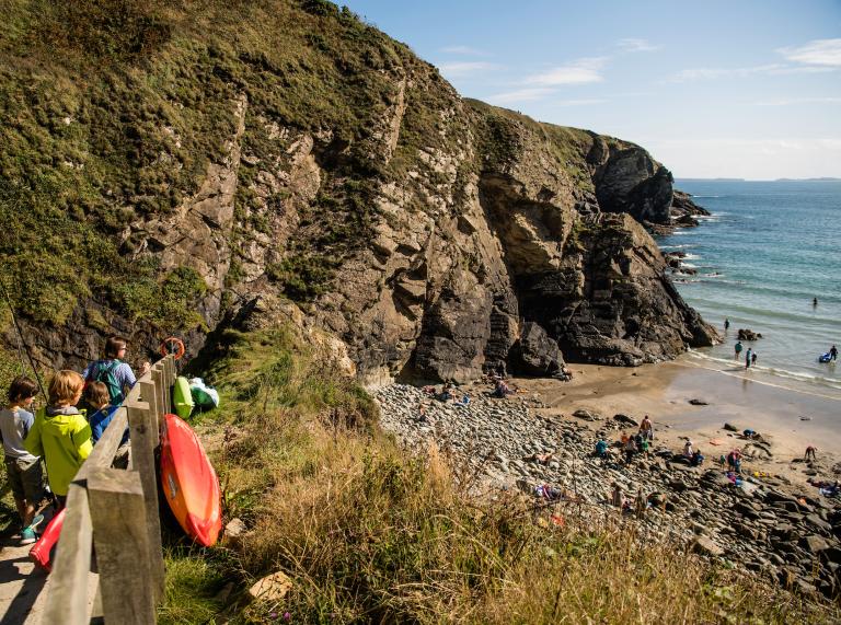 Image of Caerfai cove and beach with kayakers walking down the path to the beach