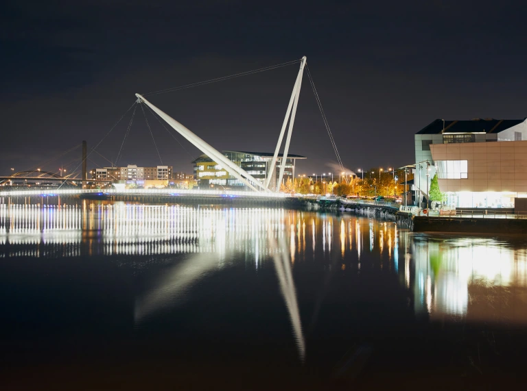 Newport city footbridge at night with lights reflecting in the water.
