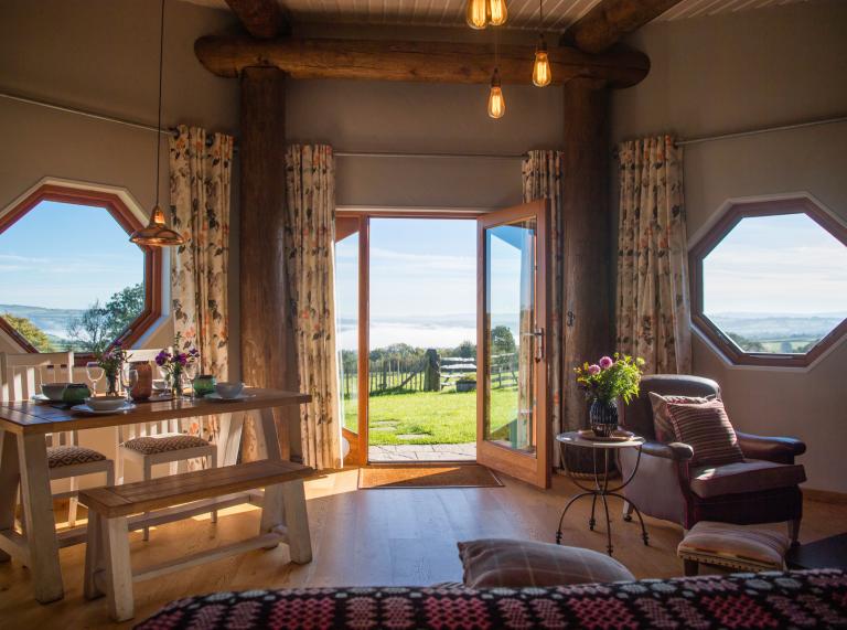 Inside a wooden eco-cabin, with patio doors opening out onto a green field. 