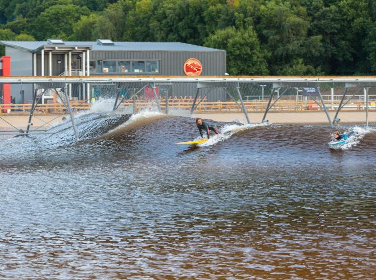 Two people taking off on a wave at Surf Snowdonia, in North Wales