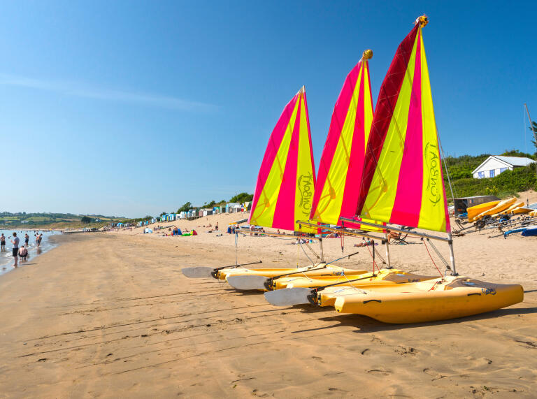 A row of red and yellow dinghies on a warm beach 