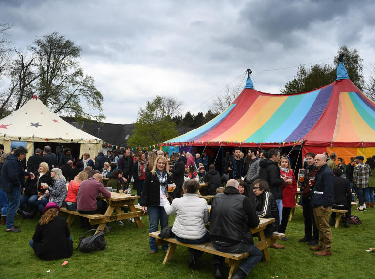 Two large colourful tents surrounded by lots of people drinking and having a nice time 