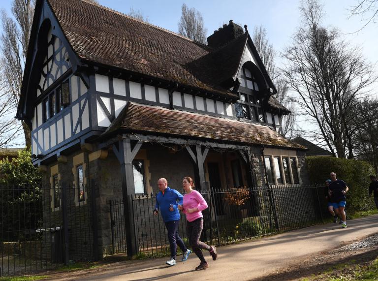 Two runners running past a Tudor house in Bute Park.
