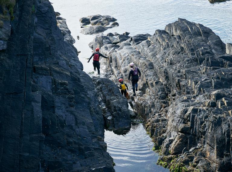Family wading through large rocks off the West Wales coastline.