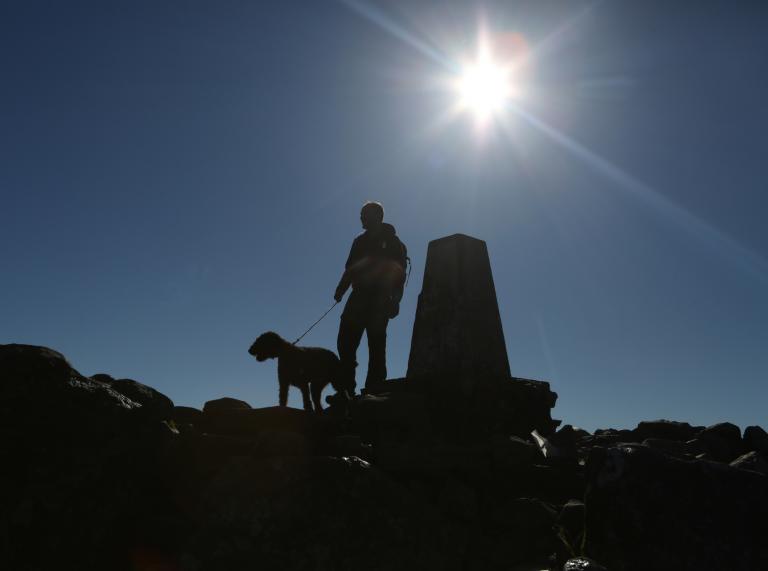 View towards the summit Penygadair, a man and a dog silhouetted on a sunny day.