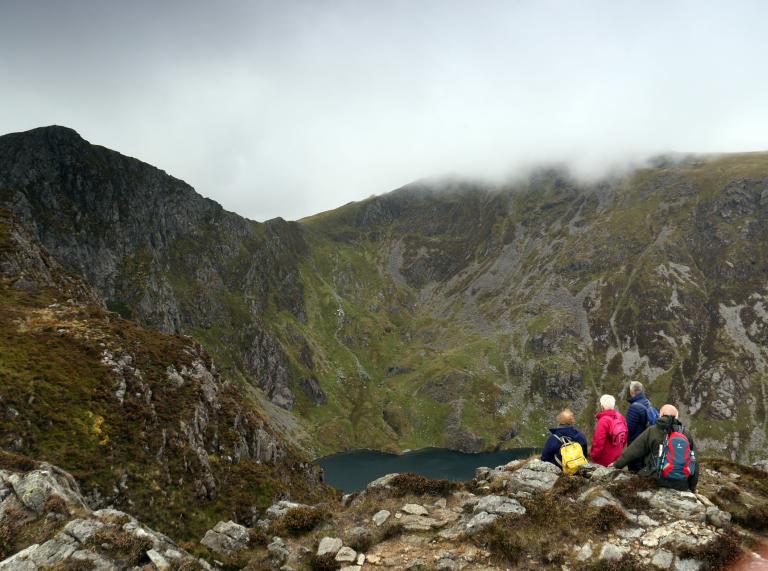 A group of people sat looking at Llyn Cau from the Minffordd Path, Cader Idris, Snowdonia with Craig Cau (left) and Penygadair (right).