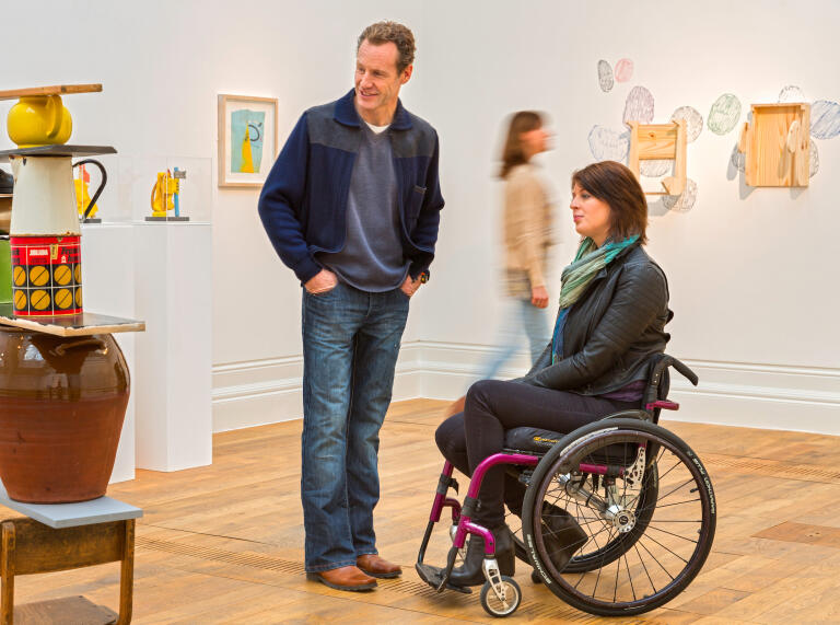 Woman using wheelchair and a standing man at an art gallery.