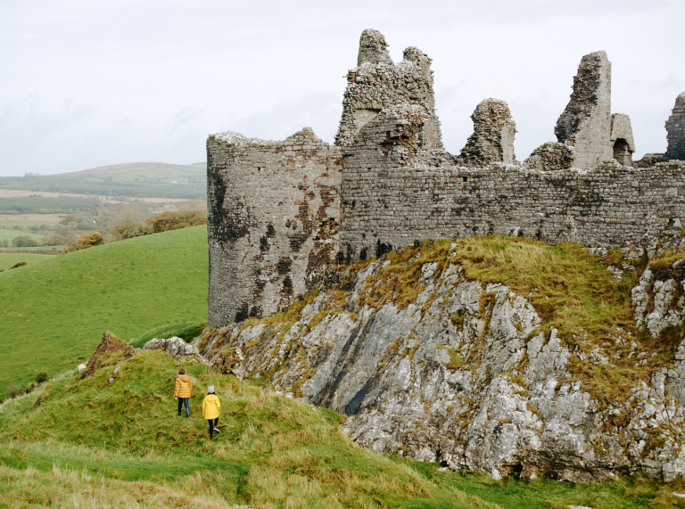 Two people exploring external stone walls of Castell Carreg Cennen.