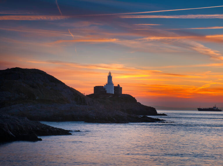 The Mumbles head lighthouse at sunrise from Bracelet Bay.