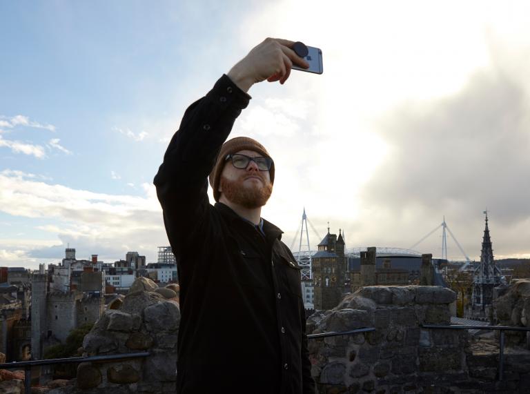 A man holds up a phone to take a selfie over a city skyline