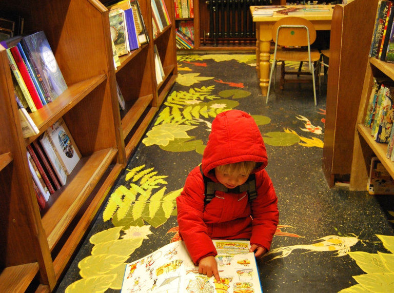 A small child reading a book on the floor of a book shop.