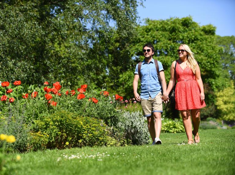 Ein Paar spaziert durch einen grünen Park mit Blumen.