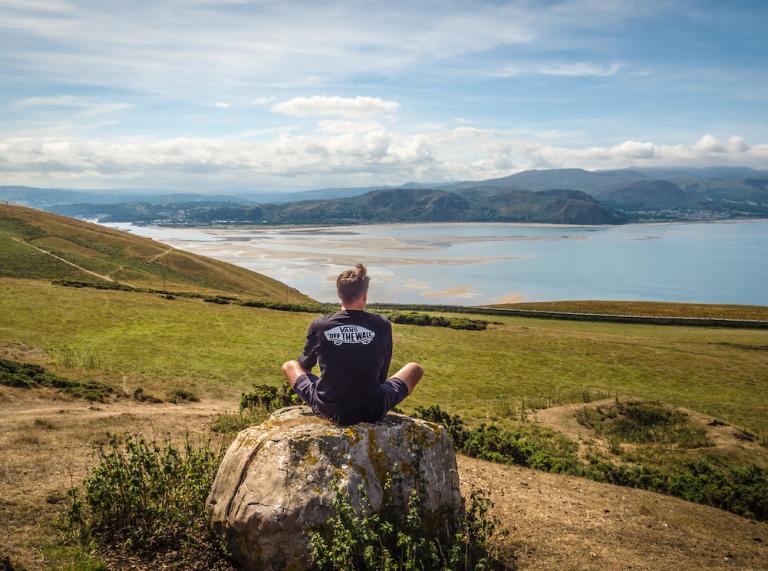 Ein Mann sitzt auf einem Felsen mit Blick auf die Landschaft und Küste.