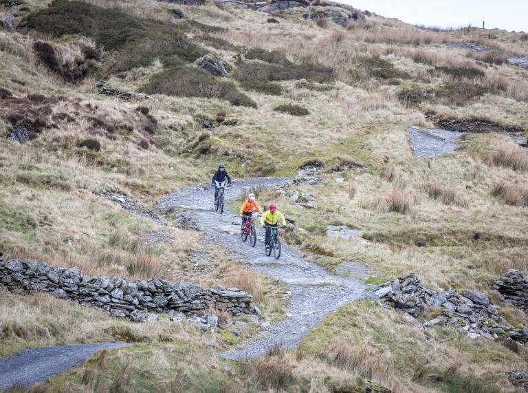 Three mountain bikers cycling down a windy mountainous trail.