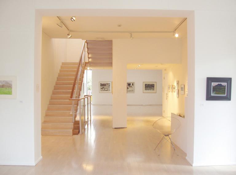 interior of a white art gallery with a staircase to the left and displays on walls