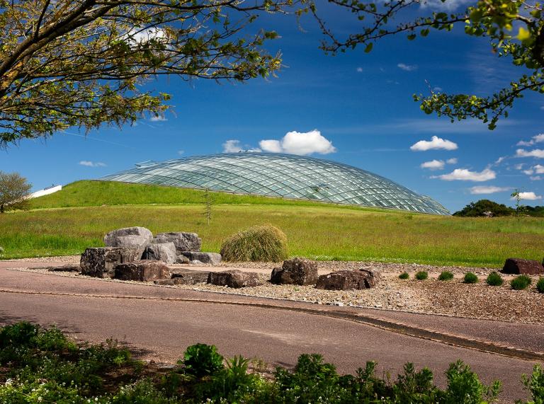 Looking towards a large glasshouse containing tropical plants over grassy bank.