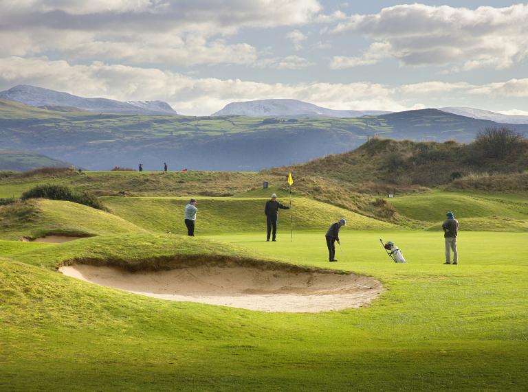 Golfers on Porthmadog golf course with mountains in the background.