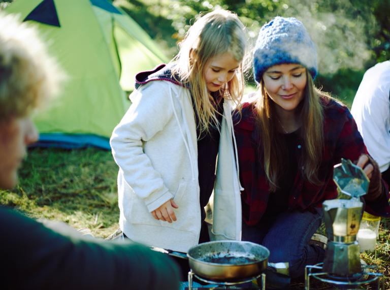 A little girl and young woman brewing coffee around a campfire.