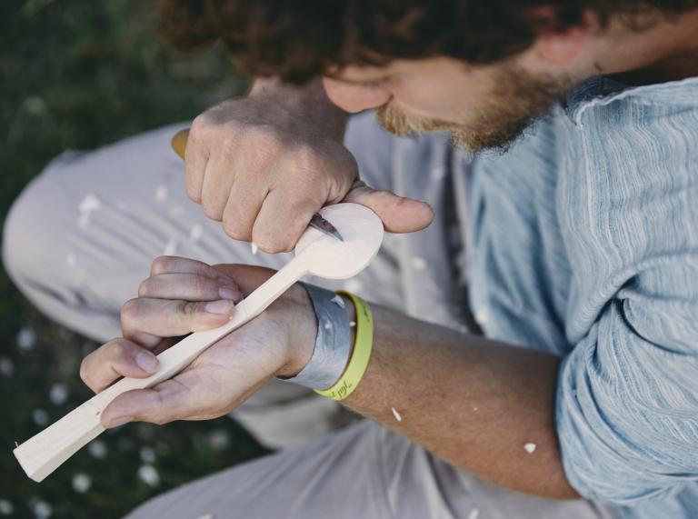 A bearded man whittling a wooden spoon.
