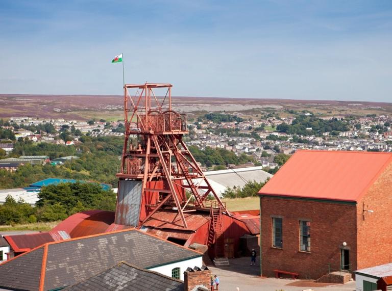 A view of a forecourt with a red pit wheel and a red building in Blaenavon.