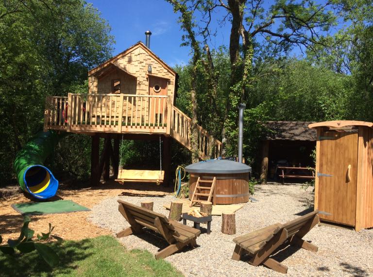 A tree house with hot tub, slide and swing seat.