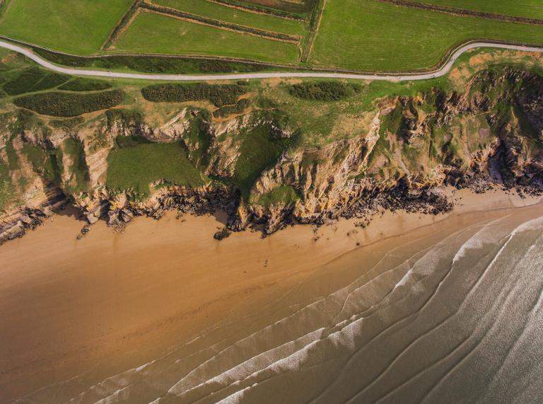 A sandy beach at the bottom of a high cliff from above.
