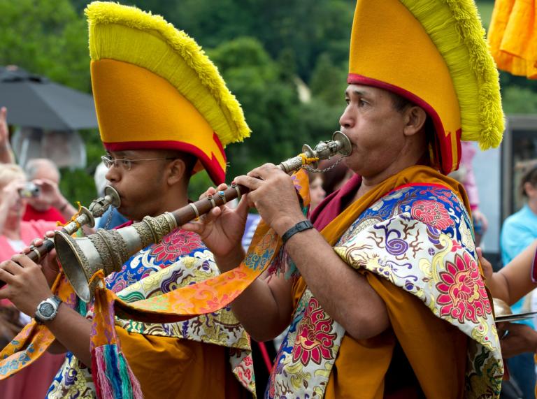 Two Tibetan monks in colourful traditional clothes playing wind instruments