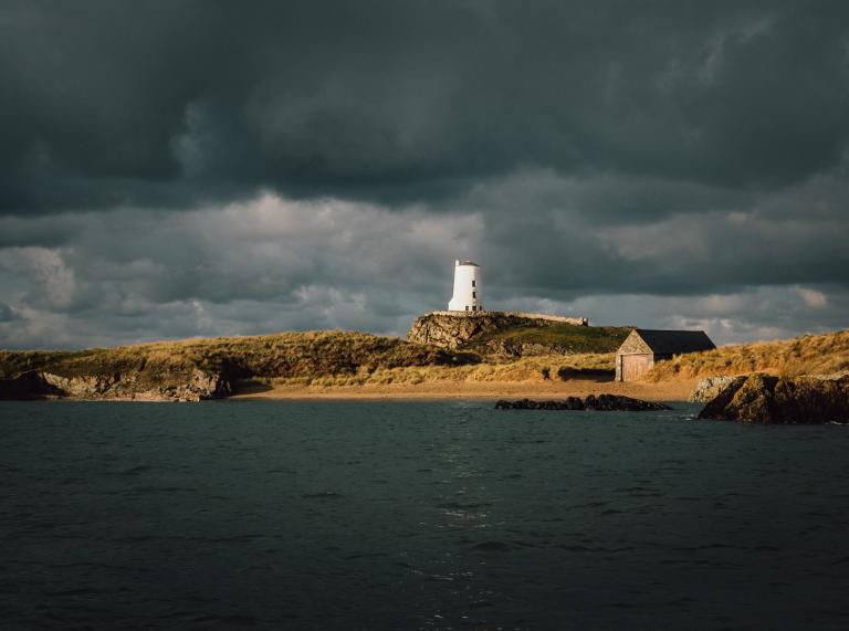 A white lighthouse on a sandy beach under stormy skies.