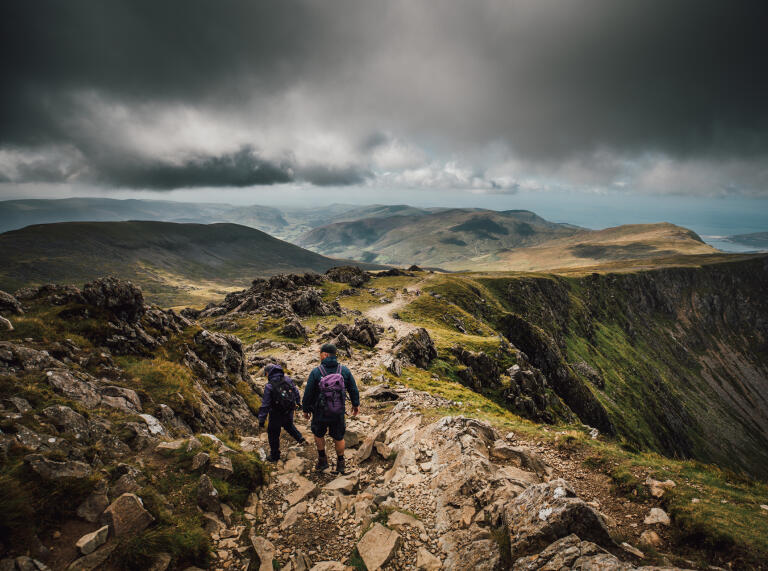 Two people walking along a mountain ridge.
